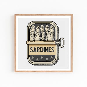 May include: A framed print featuring a stylized illustration of a sardine can. The can is open, revealing five fish. The word "SARDINES" is printed on the can, with anchor symbols below. The artwork is in black and beige tones.