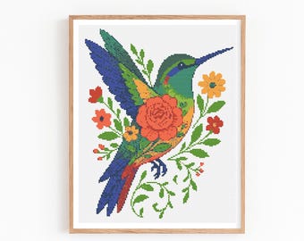 May include: A framed cross-stitch art piece featuring a colorful hummingbird. The bird is depicted with blue, green, orange, and red hues, surrounded by flowers and foliage. The artwork is set against a white background.