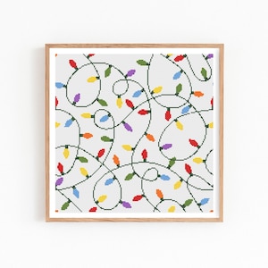 May include: A framed cross-stitch pattern featuring a repeating design of colorful Christmas lights. The lights are red, orange, yellow, green, blue, and purple, strung on green wires against a white background. The frame is made of light brown wood.
