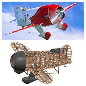 Può includere: Un aereo rosso e bianco d'epoca in volo contro un cielo blu. L'aereo ha una grande elica e il numero "7" sul lato. Sotto, è esposto un modello a telaio in legno dello stesso aereo.