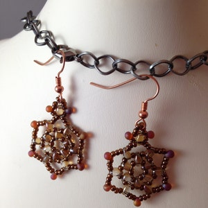 May include: A pair of brown and copper beaded earrings with a geometric design. The earrings are hanging from a copper wire and have a starburst shape.