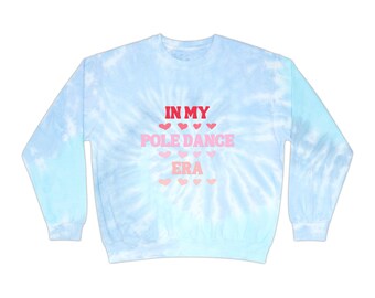 以下が含まれることがあります： ピンクのハートで囲まれた赤、ピンク、白の文字で「IN MY POLE DANCE ERA」と書かれた薄いブルーのタイダイ染めスウェットシャツです。