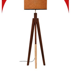 May include: A floor lamp with a dark brown wooden tripod base and a cylindrical drum lampshade featuring a woven cane texture. The lamp includes a light-coloured wrapped accent on one leg and a black power cord extending from the base.
