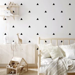 May include: A white wall with black triangle decals, a wooden shelf with a toy airplane, a wooden dollhouse, and a wooden bed with white bedding and pillows.