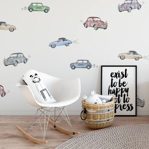 May include: A white rocking chair with a panda-themed pillow, a wicker basket with a toy inside, and a framed print with the text "exist to be happy, not to impress". The wall behind the chair is decorated with watercolor car stickers in various colors.