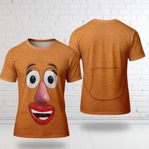 May include: A short-sleeved, orange t-shirt featuring a cartoon face with large black eyes, a pink nose, and a red smiling mouth. The back of the shirt is plain orange with a pocket design. The shirt has a textured appearance.