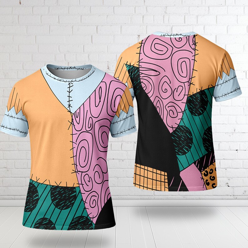 Op de afbeelding: Een t-shirt met korte mouwen met een patchwork-ontwerp met oranje, roze, zwarte en teal secties. Het shirt heeft een lichtblauwe halslijn en mouwen, met zichtbare stikdetails. Het ontwerp is zichtbaar op zowel de voor- als achterkant.