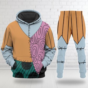 Op de afbeelding: Een tweedelige outfit met een hoodie en bijpassende broek. De hoodie heeft een patchwork ontwerp in oranje, lichtblauw, roze en zwart. De broek is oranje en lichtblauw met zwarte stikseldetails. Een uniek, opvallend ontwerp.