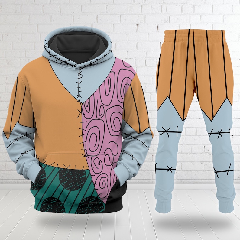 Op de afbeelding: Een tweedelige outfit met een hoodie en bijpassende broek. De hoodie heeft een patchwork ontwerp in oranje, lichtblauw, roze en zwart. De broek is oranje en lichtblauw met zwarte stikseldetails. Een uniek, opvallend ontwerp.