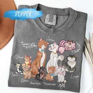 K&ouml;nnte beinhalten: Ein graues Comfort Colors T-Shirt mit einer farbenfrohen Illustration verschiedener Zeichentrickkatzen, darunter Thomas O'Malley, Duchess und Cheshire Cat. Die Namen der Katzen sind unter jeder Figur geschrieben. Das Wort "Pepper" steht oben links.
