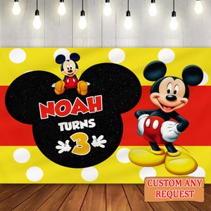 May include: A yellow and red backdrop with white polka dots and a large black Mickey Mouse head shape. The text "NOAH TURNS 3" is displayed. A cartoon Mickey Mouse character is on the right. The words "CUSTOM ANY REQUEST" are on a brown sign.