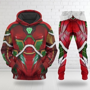 Puede incluir: Un conjunto de sudadera con capucha y pantal&oacute;n de ch&aacute;ndal rojos y verdes. La sudadera con capucha presenta un dise&ntilde;o detallado con detalles verdes y dorados, una capucha y un bolsillo delantero. El pantal&oacute;n de ch&aacute;ndal tiene un dise&ntilde;o similar con un ribete blanco en la cintura.