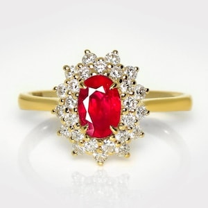 May include: A yellow gold ring featuring a central oval-cut red ruby gemstone surrounded by a halo of small, round, clear white diamonds. The band is smooth and polished, showcasing a classic design with a vibrant red stone and sparkling accents.