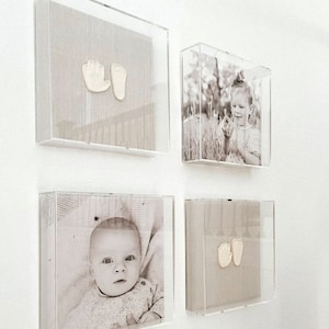 May include: Four framed images on a white wall. Two frames contain black and white photos of a child. The other two frames contain a white handprint and footprint on a beige background.