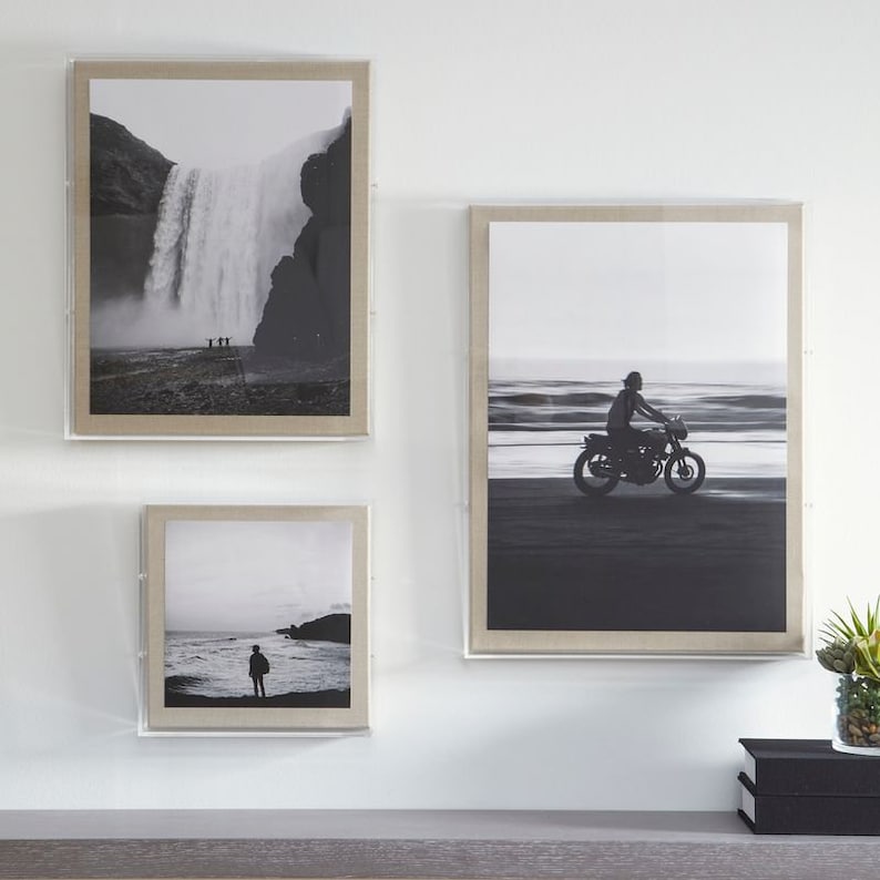 Puede incluir: Tres fotograf&iacute;as en blanco y negro enmarcadas en una pared blanca. La foto superior muestra una cascada en un paisaje monta&ntilde;oso. La foto del medio muestra a una persona conduciendo una motocicleta en una playa. La foto inferior muestra a una persona de pie en una playa.