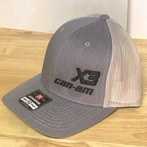 Puede incluir: Gorra de camionero gris y blanca con un logotipo bordado en negro que dice "X3 Can-Am".