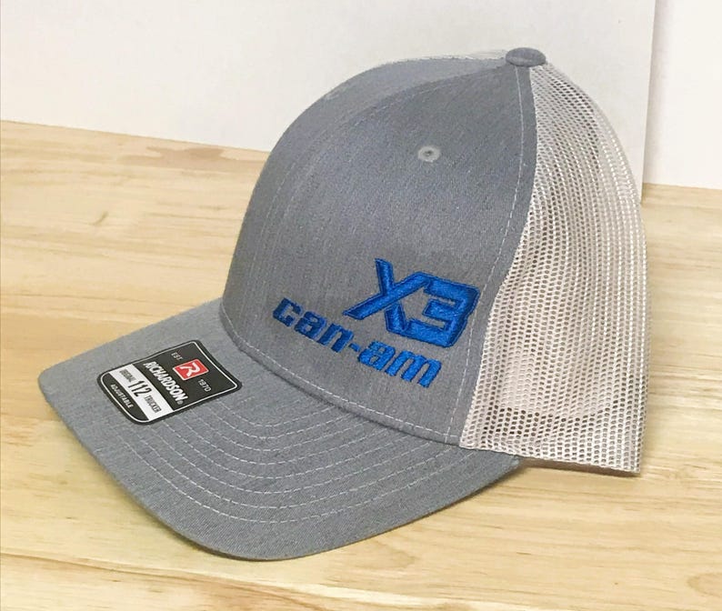 Puede incluir: Gorra de camionero de malla gris y blanca con un logotipo bordado en azul que dice "X3 Can-Am".