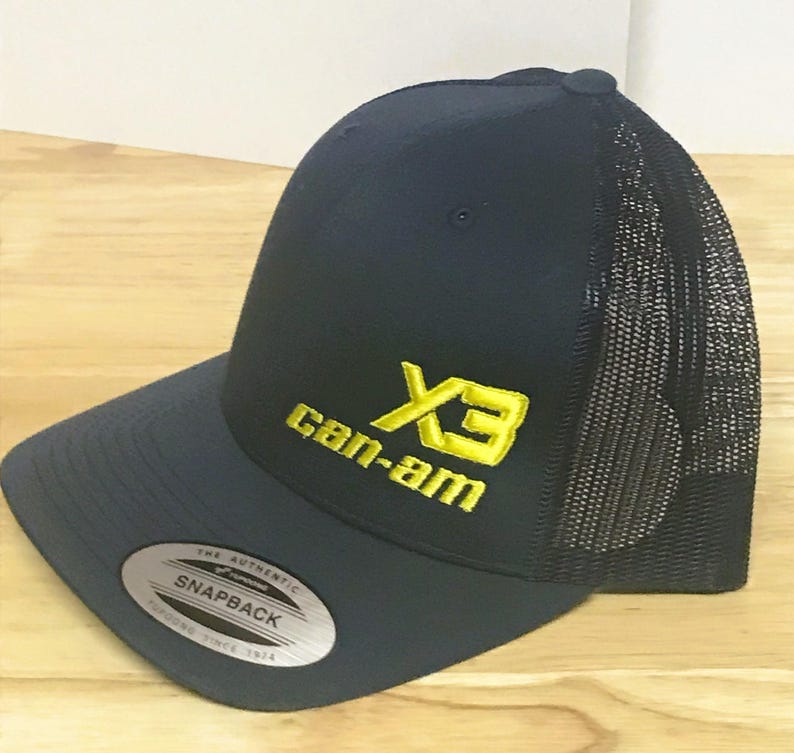 Puede incluir: Una gorra de camionero azul marino y negra con un logotipo bordado en amarillo que dice "X3 Can-Am".
