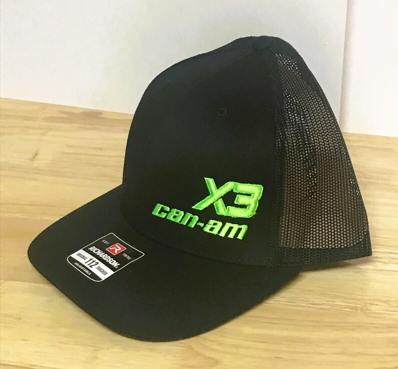 Puede incluir: Gorra de camionero negra y verde de malla con el texto "Can-Am" y un logotipo "X3" verde.