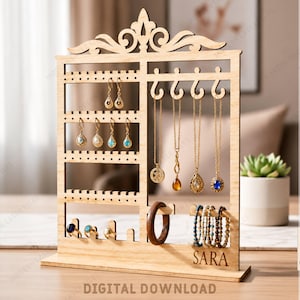 May include: A light-colored wooden jewelry organizer stand featuring a decorative top, multiple rows of holes for earrings, hooks for necklaces, and a horizontal bar for bracelets. The base is engraved with the name SARA. Text includes MATERIAL WITH 3MM, DXF, SVG, AI, EPS, PDF, and DIGITAL DOWNLOAD.