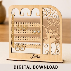 Peut inclure: Un présentoir à bijoux en bois clair avec une silhouette de ballerine découpée au laser, des motifs en volutes et des rangées horizontales avec des encoches pour boucles d'oreilles et colliers. La base porte le nom Julia. Matériau avec 3mm.