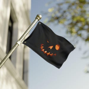Op de afbeelding: Zwarte Halloween-vlag met een uitgesneden pompoengezicht-ontwerp. De rechthoekige vlag heeft een lachend pompoengezicht met oranje en gele details. De vlag is bevestigd aan een zilveren paal en wappert in de wind.