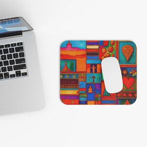 Op de afbeelding: Een rechthoekige muismat met een kleurrijk, abstract ontwerp. Het ontwerp bevat verschillende vormen en patronen in tinten rood, oranje, blauw en groen. Een witte computermuis ligt op de mat, naast een laptop.