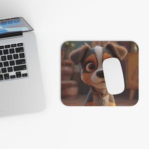 Op de afbeelding: Een rechthoekige muismat met een cartoon puppy met bruin, zwart en wit haar en grote bruine ogen. Een witte computermuis ligt op de muismat. De achtergrond is wazig.