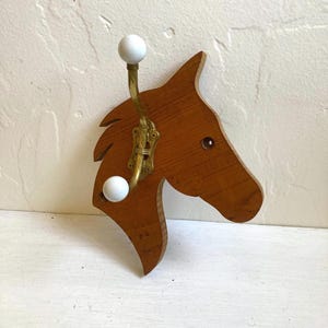 May include: Wooden horse head wall hook with brass hardware and two white ball knobs. The horse head is made of stained wood and has a carved design. A decorative and functional item.