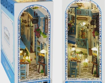 May include: A detailed miniature diorama depicting a Mediterranean village scene, with blue and white buildings, cobblestone streets, and small tables and chairs. The box has the text "Sea Breeze".