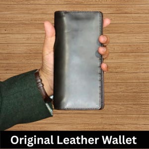 Könnte beinhalten: Ein schwarzes Lederportemonnaie wird in einer Hand gehalten. Das rechteckige Portemonnaie hat eine glatte Oberfläche und sichtbare Nähte. Der Text "Original Leather Wallet" wird in einem schwarzen Balken unten angezeigt.