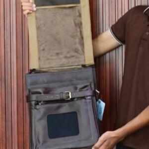 Może przedstawiać: Ciemnobrązowa sk&oacute;rzana torba kurierska z klapą i klamrą. Torba ma prostokątny kształt z przednią kieszenią i małym okienkiem. Wnętrze jest wyłożone beżową tkaniną.