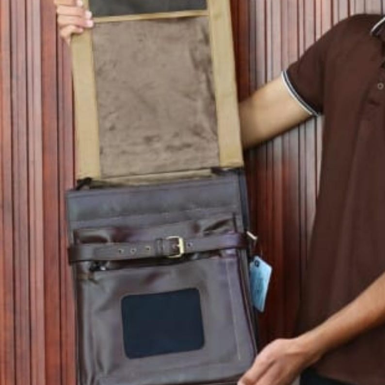 Może przedstawiać: Ciemnobrązowa sk&oacute;rzana torba kurierska z klapą i klamrą. Torba ma prostokątny kształt z przednią kieszenią i małym okienkiem. Wnętrze jest wyłożone beżową tkaniną.