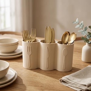 Op de afbeelding: Een beige bestekorganizer met drie vakken gemaakt van glad materiaal. Elk gedeelte is aan de voorzijde voorzien van een verhoogd, in reliëf aangebracht icoon van een vork, mes of lepel. De organizer bevat goudkleurige vorken, messen en lepels.
