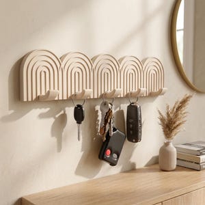 Könnte beinhalten: Ein beigefarbenes Wand-Schlüsselbrett mit fünf gewölbten, gerippten Segmenten und integrierten Haken. Drei Metallschlüsselbunde und ein schwarzer elektronischer Funkschlüssel hängen an den Haken. Das Regal hat eine matte Oberfläche.