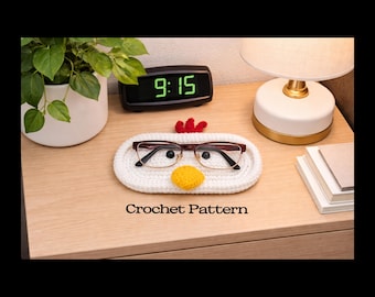 May include: An oval white crochet tray featuring a red crest and a yellow beak, designed to hold eyeglasses. The tray has two small black circular eyes and is displayed with a pair of glasses resting on it. The text Crochet Pattern is visible.