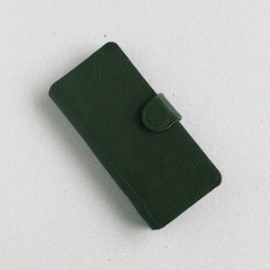 A dark green sustainable leather flip-cover for a smartphone on a light grey background.