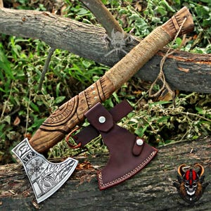 May include: A hand axe with a carved wooden handle wrapped in twine, featuring a metal head engraved with intricate Norse-inspired patterns and a circular symbol. A dark brown leather sheath with silver-toned metal snaps covers the axe blade.