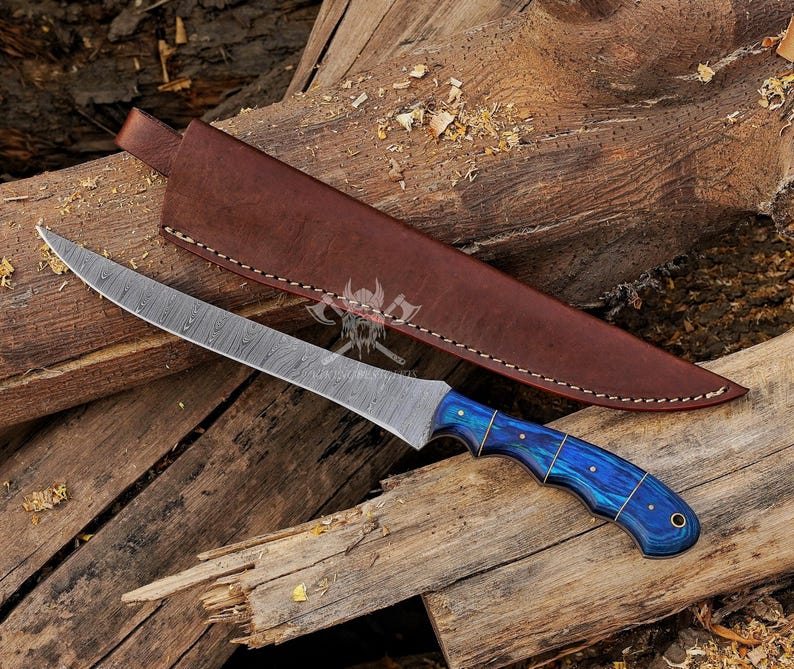 May include: A Damascus steel knife with a curved blade and a blue and gold handle, resting on a wooden surface. The knife is accompanied by a brown leather sheath. The blade has a unique pattern, and the handle has a vibrant blue hue.
