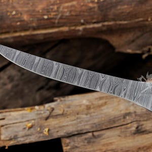 May include: A curved, Damascus steel blade knife with a wooden handle. The blade has a unique, patterned design. The handle is dark brown with brass rivets. The knife is set against a rustic wooden background.