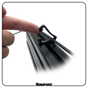 May include: A black plastic cable management clip attached to a black aluminum extrusion profile. The clip features an open hook design to secure a thin black cable. The component is matte black with a rigid structure, designed for cable organization.