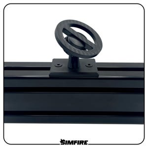 Puede incluir: Un componente negro en forma de volante montado sobre una base negra, fijado a un riel negro ranurado. El componente tiene un diseño circular con un cubo central y una estructura exterior en forma de anillo. El logotipo de Simfire está en la parte inferior.