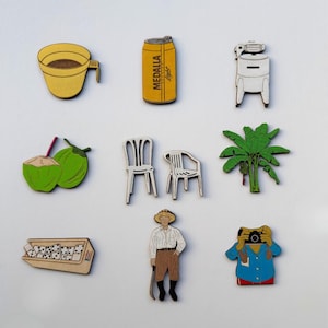 May include: A collection of wooden magnets featuring various designs. Includes a yellow coffee cup, a can of Medalla Light, a white appliance, two green coconuts with straws, two white chairs, a green palm tree, a domino set, a person with a hat and a camera-holding figure.