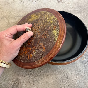 May include: A round wooden box with a black interior and a floral design on the lid. The lid has a small metal knob.