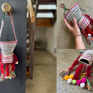 May include: A silver and pink beaded hanging ornament with red and white tassels. The ornament is decorated with colorful pom-poms.