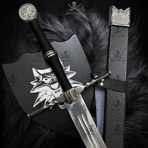 May include: A silver and black sword with a twisted handle, a black grip, and a wolf emblem on the pommel. The sword is displayed with a black shield featuring a wolf's head and a black sheath.