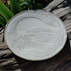 May include: A white ceramic plate featuring an embossed design of a bird with outstretched wings. The plate has a subtle grey glaze.
