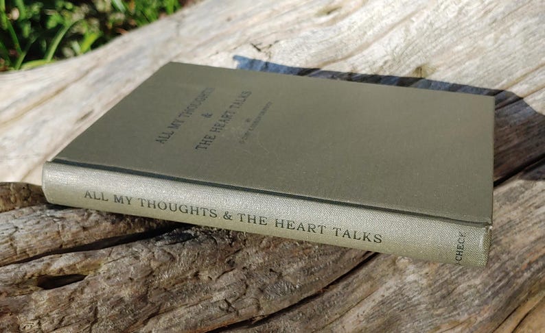 Puede incluir: Un libro de tapa dura titulado "ALL MY THOUGHTS & THE HEART TALKS" en un color verde apagado. El libro est&aacute; sobre una superficie de madera envejecida, con el texto del t&iacute;tulo visible en el lomo y la portada. Los bordes del libro est&aacute;n ligeramente desgastados.