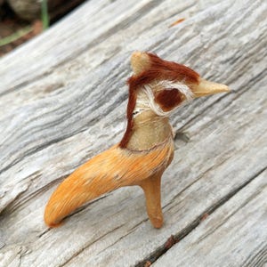 May include: A small, handmade animal figurine made from bone and fur. The figurine is brown, white, and orange and has a long neck and beak. It is standing on a wooden surface.