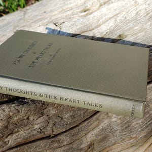 Puede incluir: Un libro de tapa dura verde apagado titulado "ALL MY THOUGHTS & THE HEART TALKS" sobre una superficie de madera envejecida. El t&iacute;tulo est&aacute; impreso en un color m&aacute;s oscuro. El lomo del libro tambi&eacute;n muestra el t&iacute;tulo.